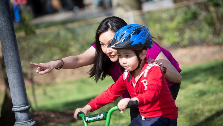 A photo of a mother teaching her son to ride a bicycle